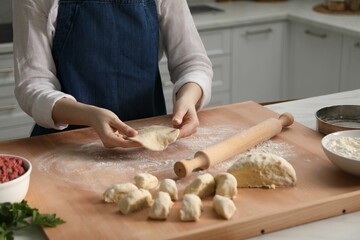 Making khinkali. Woman shaping piece of dough at table in kitchen, closeup