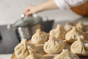 Woman with many uncooked khinkali near cooktop in kitchen, closeup