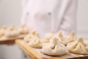 Chef holding board with uncooked khinkali indoors, closeup