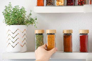 Woman taking glass jar of spices from shelf indoors, closeup