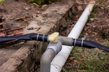 Close-up of outdoor plumbing or irrigation pipes and a valve on the ground. Represents...