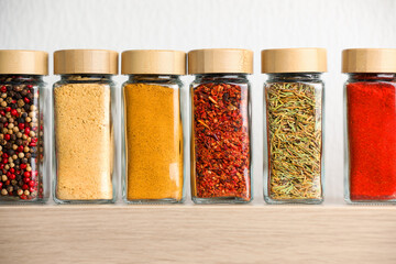 Different aromatic spices in jars on wooden shelf indoors, closeup