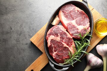 Pieces of raw beef meat with spices in baking dish and oil on gray textured table, flat lay. Space for text