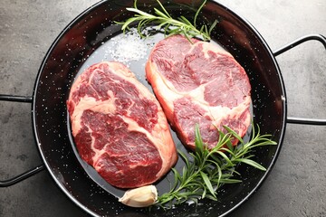 Pieces of raw beef meat and spices in baking dish on gray textured table, top view