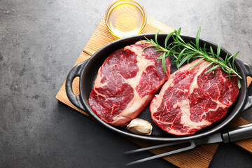 Pieces of raw beef meat with spices in baking dish, oil and fork on gray textured table, flat lay