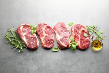 Pieces of raw beef meat and spices on grey table, flat lay