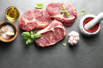 Pieces of raw beef meat and spices on grey table, flat lay. Space for text