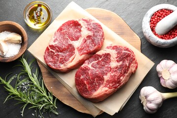 Pieces of raw beef meat and spices on black table, flat lay