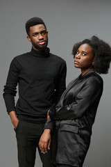 Stylish young African couple in black attire expressing confidence against a neutral gray background, showcasing contemporary fashion and modern emotions