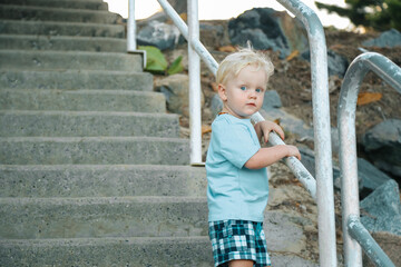Little boy holding rail on concrete stairs leading to the beach