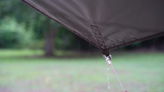 rainy season camping with heavy rain water drips droplets to tip tarp and flow motion on fly sheet tent with carabiner paracord rope umbrella by holiday travel on nature forest garden with rain sound