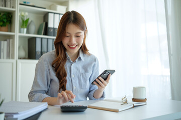 Smiling businesswoman calculating expenses and using smartphone at desk.