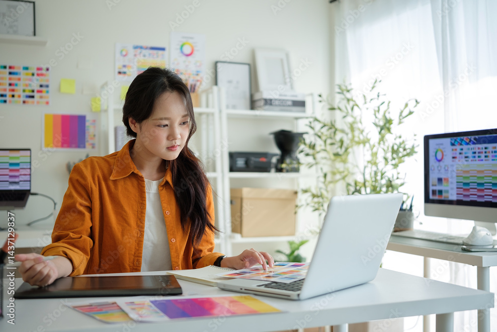 Poster designer analyzing printed color samples while working on a project at her workstation.