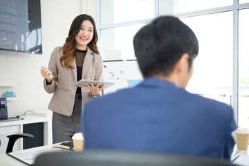 Smiling businesswoman in a beige suit presenting ideas with a digital tablet during a team meeting in a modern office.