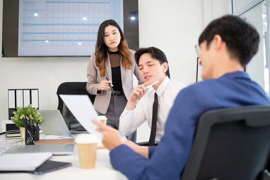 Group of coworkers exchanging ideas while reviewing printed charts at a desk, engaged in focused corporate discussion.