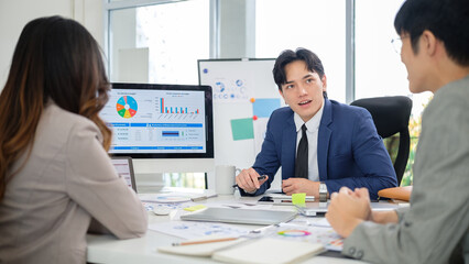 Confident male executive presenting ideas to coworkers during a collaborative meeting with visual financial summaries on display.