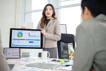 Businesswoman presenting a budget summary and expense report to colleagues using visual data on a desktop monitor.