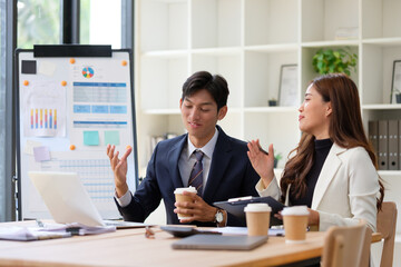 Business professionals having a dynamic discussion in front of a presentation board, surrounded by digital devices and documents.