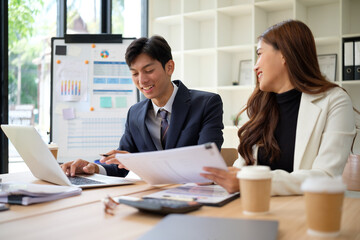 Professional colleagues discussing financial charts and data at a meeting table, smiling and engaged in teamwork.