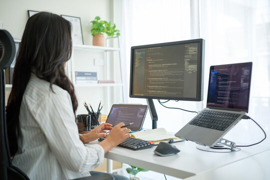 Woman using external keyboard and stylus, programming across a three-screen workstation in home office.