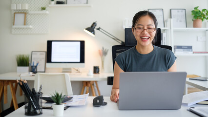 Smiling young businesswoman wearing glasses, working at her laptop in a bright home office.