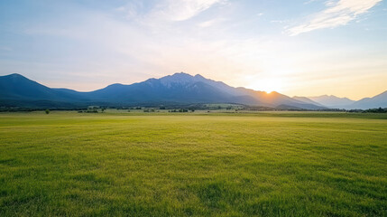 Fototapeta premium Serene landscape featuring vast green field with distant mountains under warm sunset glow