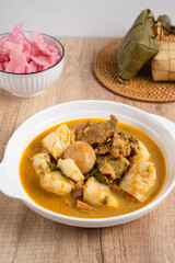 Ketupat Sayur Padang is one of the mainstay dishes from Minang, West Sumatra, Indonesia, served on a white plate with additional coconut curry sauce and jackfruit vegetables, boiled eggs, and rendang.