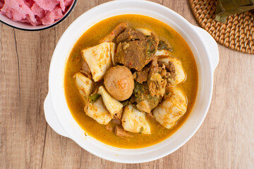 Ketupat Sayur Padang is one of the mainstay dishes from Minang, West Sumatra, Indonesia, served on a white plate with additional coconut curry sauce and jackfruit vegetables, boiled eggs, and rendang.