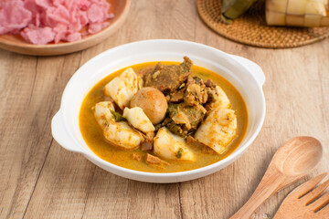 Ketupat Sayur Padang is one of the mainstay dishes from Minang, West Sumatra, Indonesia, served on a white plate with additional coconut curry sauce and jackfruit vegetables, boiled eggs, and rendang.