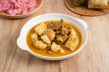 Ketupat Sayur Padang is one of the mainstay dishes from Minang, West Sumatra, Indonesia, served on a white plate with additional coconut curry sauce and jackfruit vegetables, boiled eggs, and rendang.