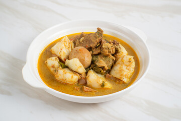 Ketupat Sayur Padang is one of the mainstay dishes from Minang, West Sumatra, Indonesia, served on a white plate with additional coconut curry sauce and jackfruit vegetables, boiled eggs, and rendang.