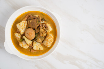 Ketupat Sayur Padang is one of the mainstay dishes from Minang, West Sumatra, Indonesia, served on a white plate with additional coconut curry sauce and jackfruit vegetables, boiled eggs, and rendang.
