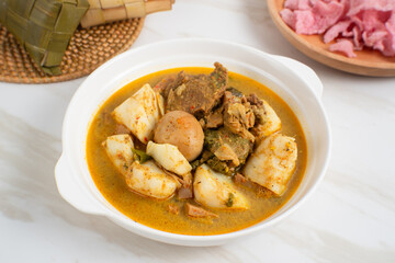Ketupat Sayur Padang is one of the mainstay dishes from Minang, West Sumatra, Indonesia, served on a white plate with additional coconut curry sauce and jackfruit vegetables, boiled eggs, and rendang.