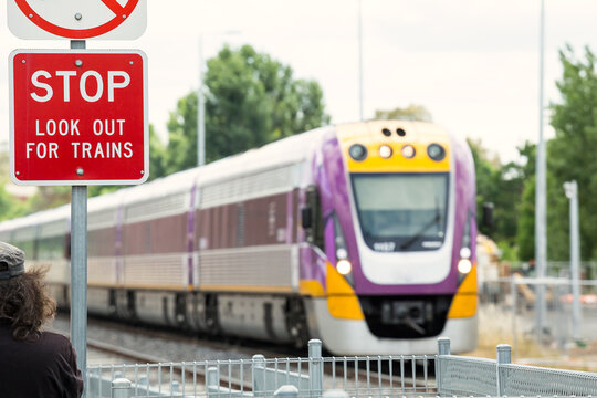 A warning sign in front of a commuter train as it approaches a pedestrian crossing
