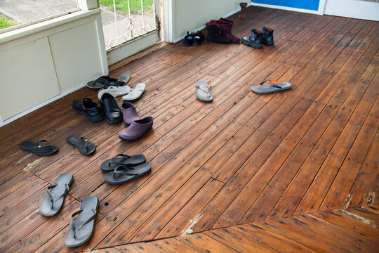 Thongs, boots and shoes scattered on deck near front door of farm house