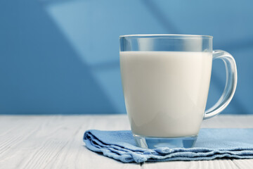 Glass mug brimming with fresh milk, resting on blue napkin atop white wooden table