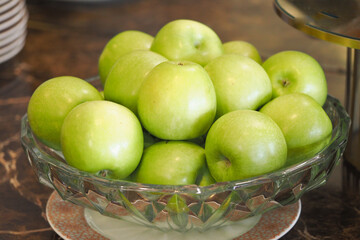 Fresh green apples arranged in a crystal bowl on a countertop