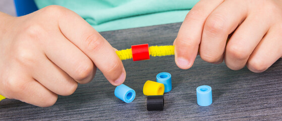 Preschooler hands with creative sticks and beads used to making bracelets. Development of kids motor skills, coordination and logical thinking