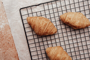 Fresh croissants cooling on wire rack on parchment and stone background