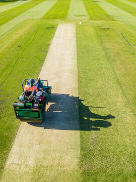 Looking down on a greens keeper riding a roller over a cricket pitch