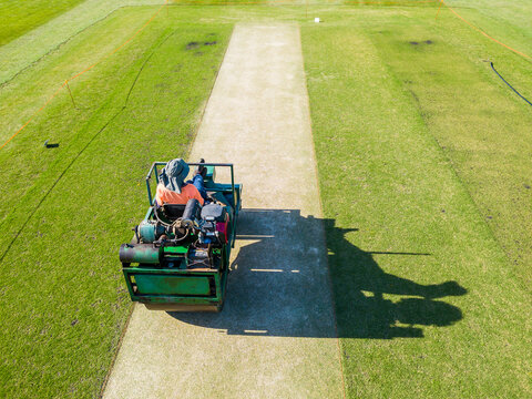 Looking down on a greens keeper riding a roller over a cricket pitch