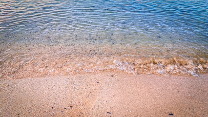 Soft waves gently washing over sandy beach under natural sunlight.
