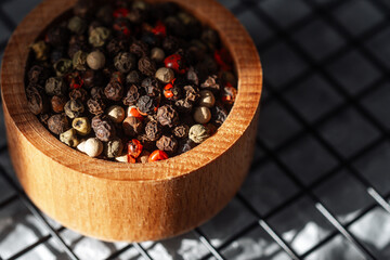 Varied peppercorns in a wooden bowl resting on a metal grid