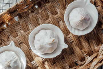 Garlic bulbs in small white bowls arranged on a woven basket