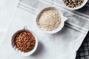 Different seeds displayed in small bowls on a kitchen towel during meal prep