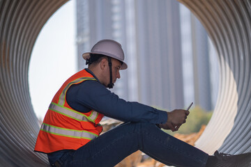 Engineer worker operations construction plans large black drainage pipe installing underground...