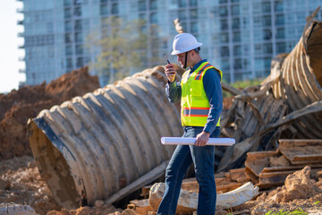 Engineer worker operations construction plans large black drainage pipe installing underground...