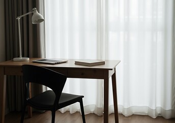 A simple desk setup with a lamp, laptop, book, and chair in front of a bright window with curtains
