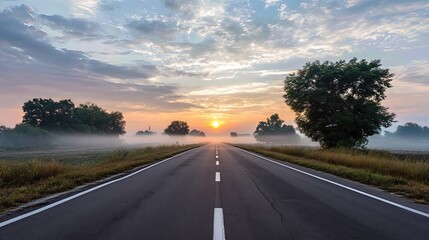 Fototapeta premium A long, empty road stretches toward the misty sunrise, symbolizing the beginning of a fresh journey.