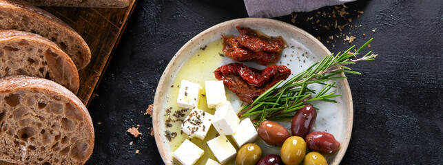 Olive oil and olives in bowls, sliced bread and rosemary on cutting board.